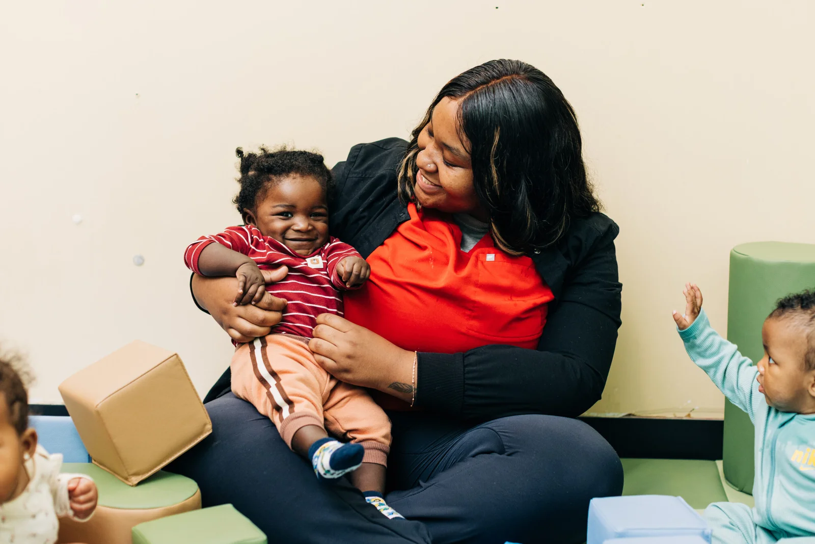 Teacher holding infant, looking at them and smiling.