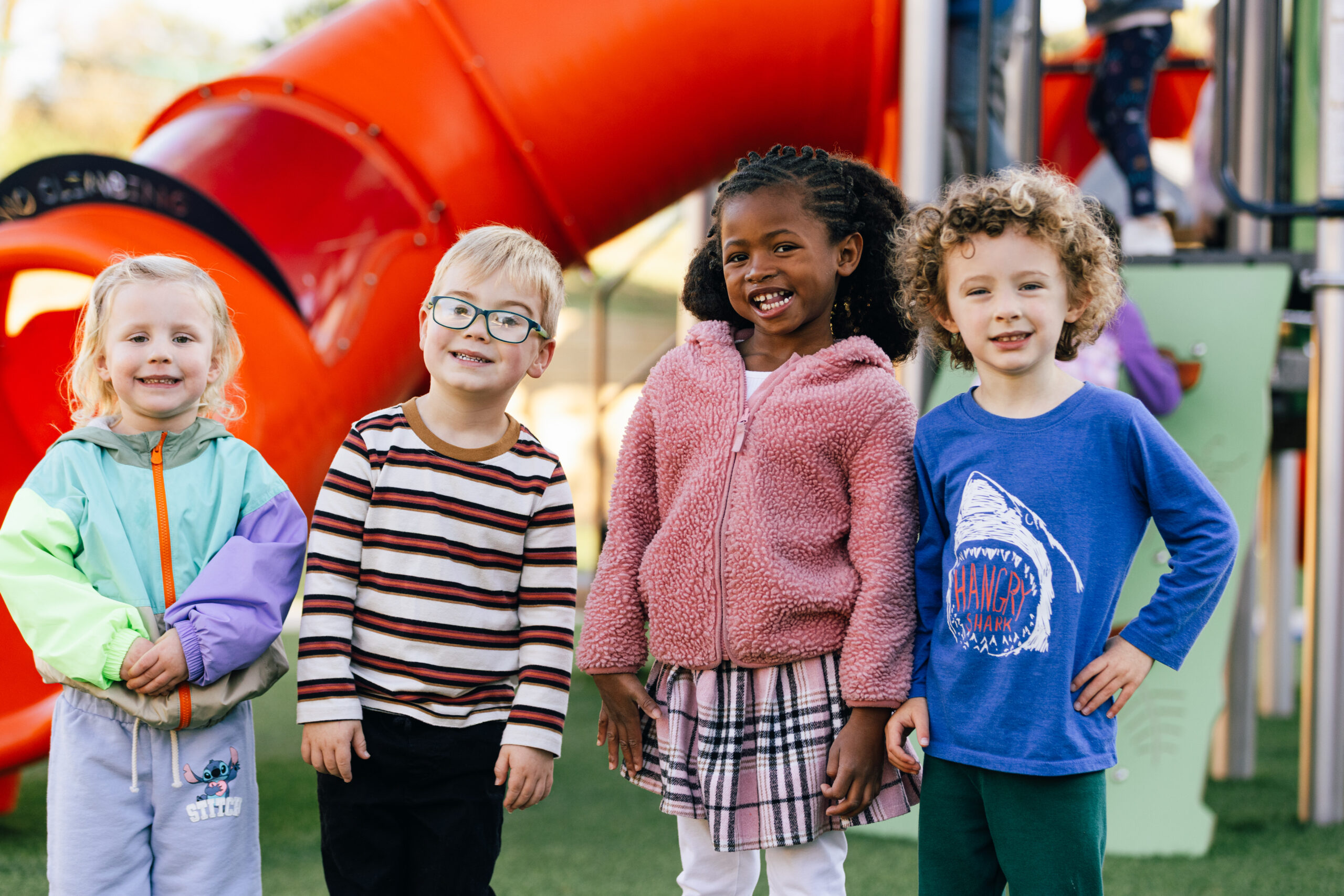 Four kids outside smiling at a playground
