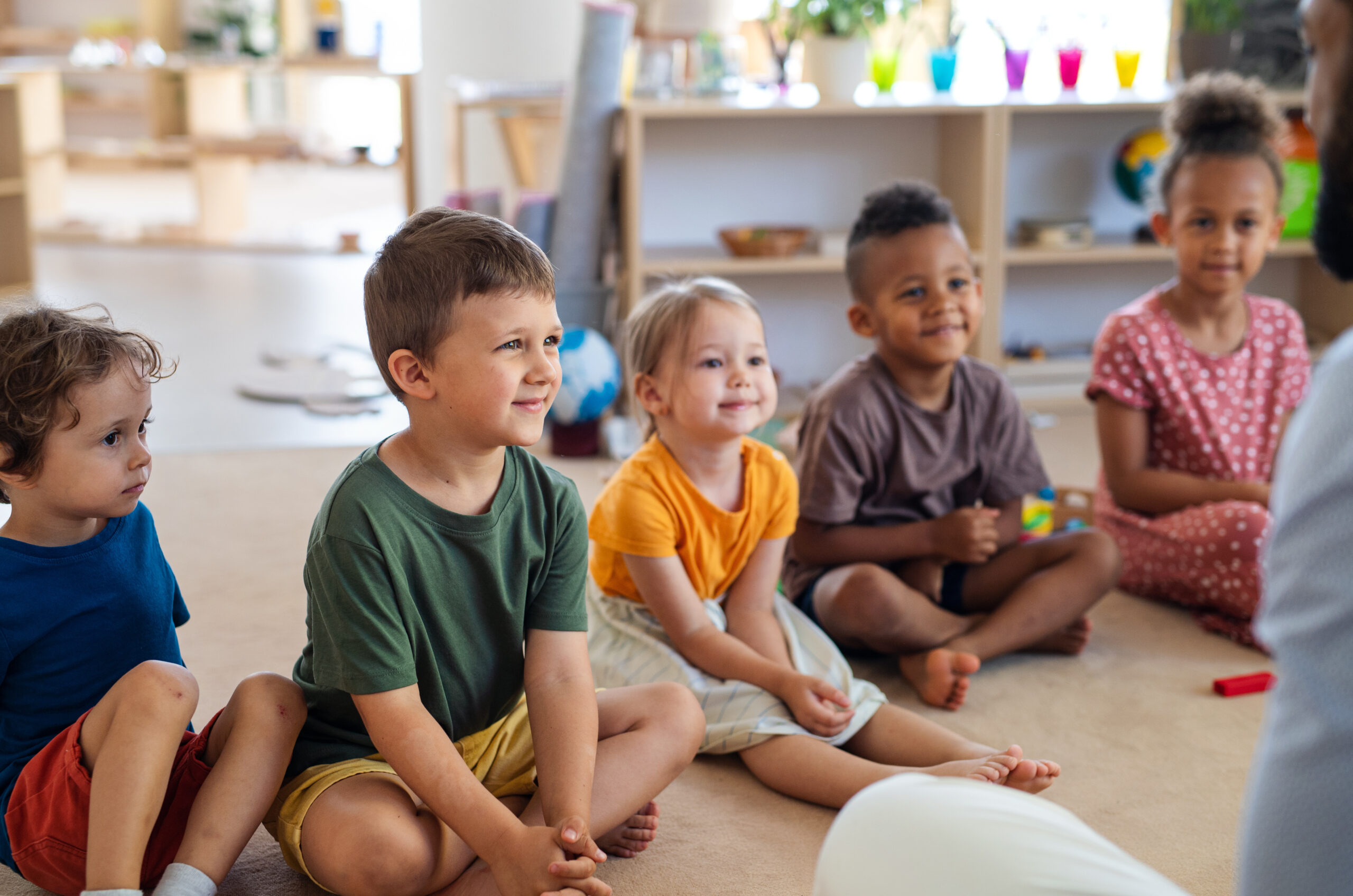 A group of small school children sitting on floor indoors in classroom.